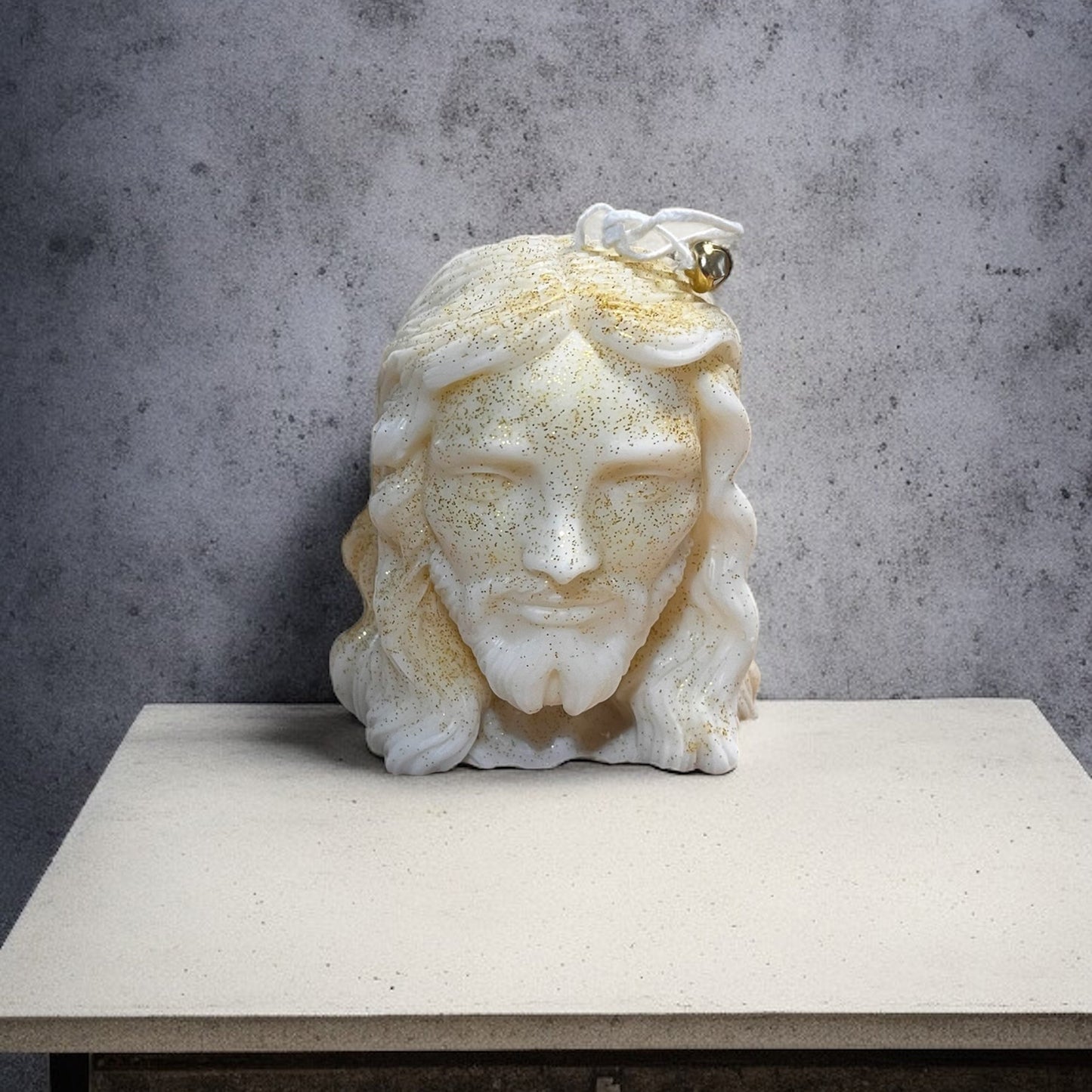 Candela artigianale raffigurante il volto di Gesù, in cera vegetale bianca con dettagli dorati e finitura luminosa.