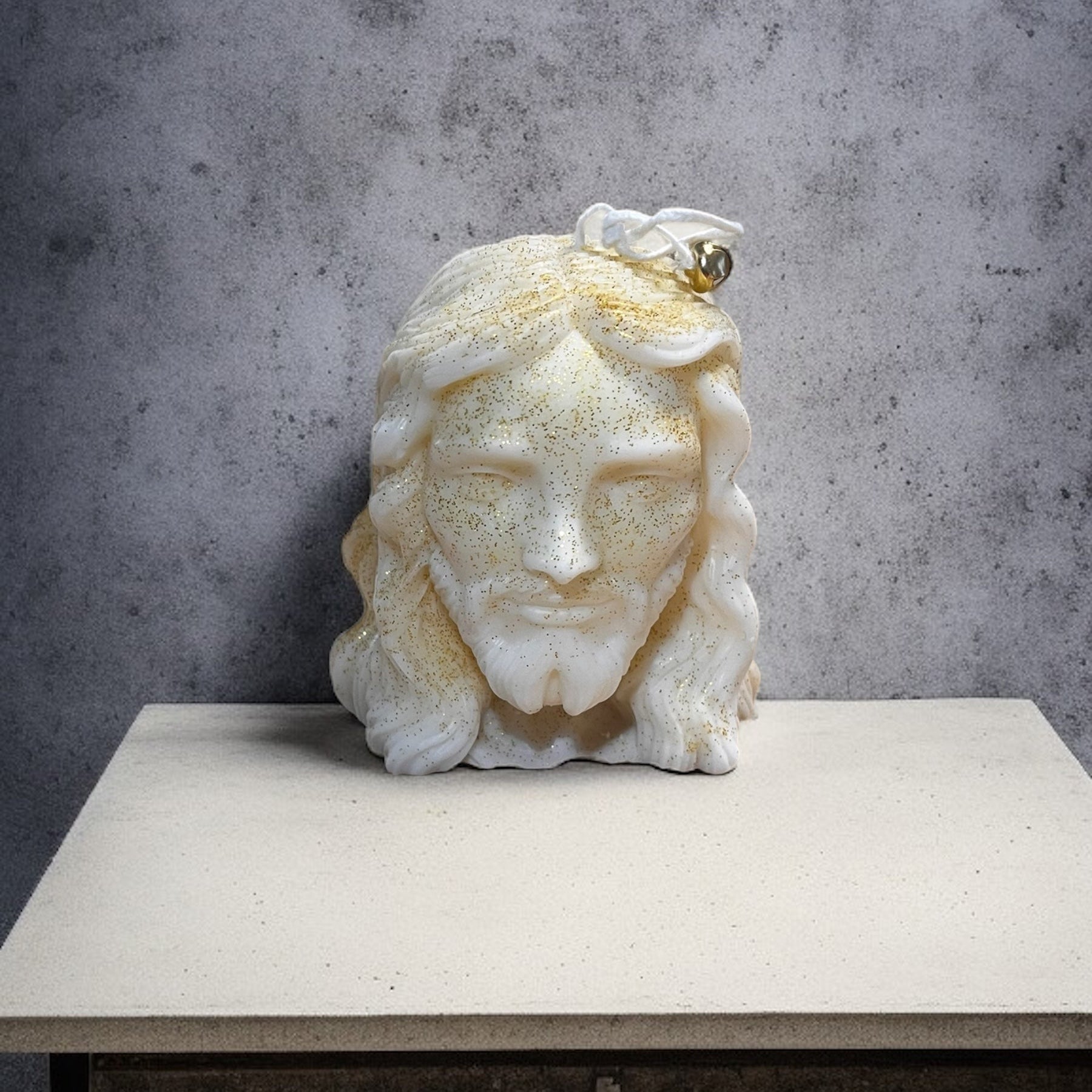 Candela artigianale raffigurante il volto di Gesù, in cera vegetale bianca con dettagli dorati e finitura luminosa.