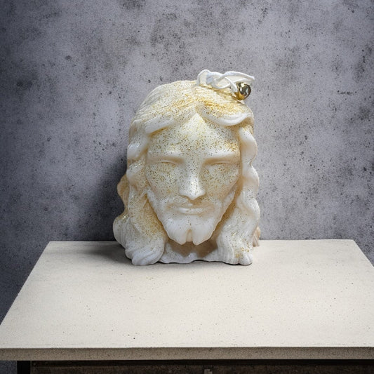 Candela artigianale raffigurante il volto di Gesù, in cera vegetale bianca con dettagli dorati e finitura luminosa.